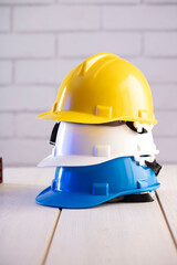 Contractor theme. Equipment of the contractor: yellow, white and blue hardhats, libella, hand saw. Plans and notebook on the white desk. White wall background.