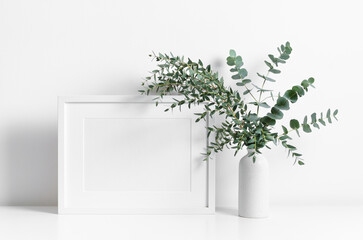 Landscape frame mockup in white room interior with fresh eucalyptus plant in vase