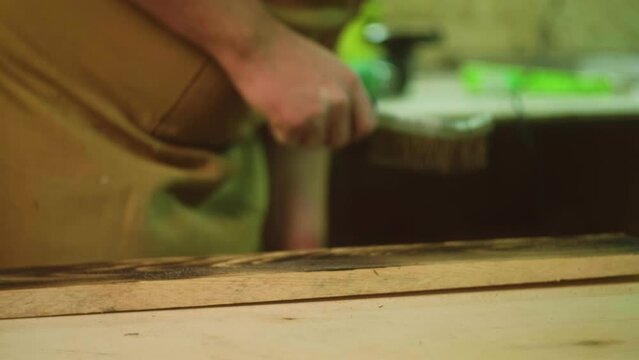 A mature carpenter makes works in his carpentry workshop, grinds wood with a brush