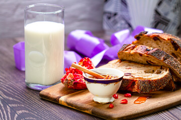 Honey, pomegranate, milk and bread on a wooden cutting board. Food photography.