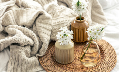 Home composition with flowers in vases and a knitted element.