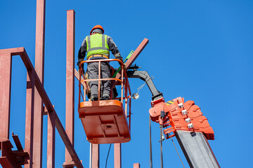 Male builders work at height in a lifting cradle, creating the iron frame of the building.