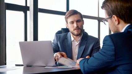 Fototapeta premium Two colleagues in suits talking at the desk