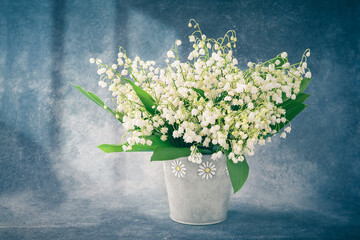 Bouquet of lily of the valleys in a vase on a blue backdrop. Holiday background. Selective focus