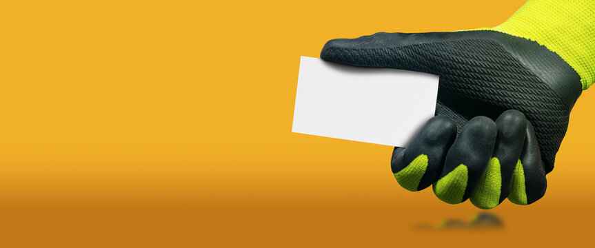 Manual worker with green and black protective work gloves holding a blank business card with copy space, on a yellow and orange background with copy space and reflections.