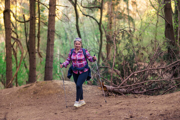 A mature woman in her 50s walks in the mountains. Use hiking poles.