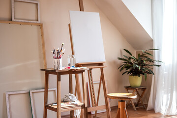 Painting art studio at loft apartment. Empty cozy workplace. Clear canvas on easel and paintbrush...