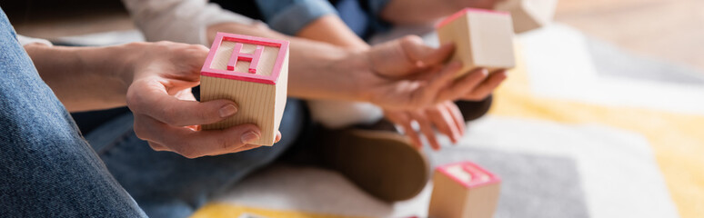 Cropped view of logopedist holding wooden block with letter near blurred child in consulting room,...
