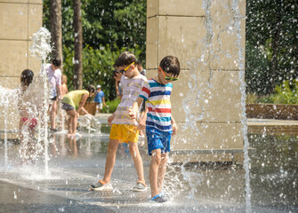 Boy having fun in water fountains. Child playing with a city fountain on hot summer day. Happy kids...