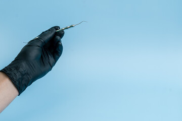 Cropped shot of professional dentist in black medical gloves with dental tool. Dental concept. Isolated on blue background