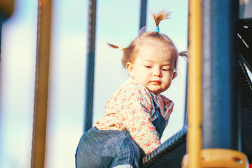Baby has multi-colored short pigtails. Active games for children. The kid is learning to climb stairs. Funny girl with pigtails on a children's slide. Happy child is playing on the playground