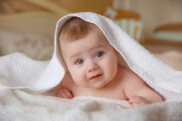 baby girl in a white towel or blanket in a white bedroom. A newborn baby is resting in bed. Portrait of a Caucasian child. The concept of kindergarten and infancy.	children's goods