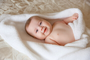 baby girl in a white towel or blanket in a white bedroom. A newborn baby is resting in bed. Portrait of a Caucasian child. The concept of children's goods
