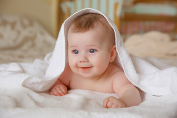 baby girl in a white towel or blanket in a white bedroom. A newborn baby is resting in bed. Portrait of a Caucasian child. The concept of children's goods