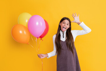 cheerful child with party helium balloons on yellow background