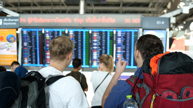 Two travel men with backpack stands back and looks schedule on scoreboard airport. concept of air travel.