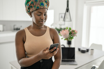 Black African woman home looking at smartphone, traditional headscarf
