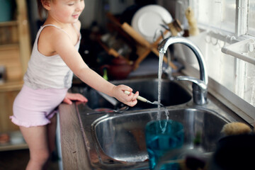 Toddler child washes his hands and fork in the sink in the kitchen, lifestyle in a real interior