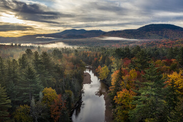 An autumn scene with a river flowing through a natural forest with green conifers and maple trees in full fall colors, Swift River, White Mountain NF, New Hampshire