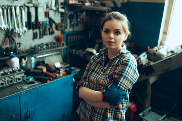 Portrait of young confident girl wearing working clothes standing at auto service station, indoors....