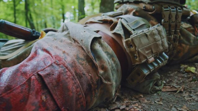 Close up leg soldier in camouflage uniform lying wounded blood around trying move near tree. In forest. War. Military concept