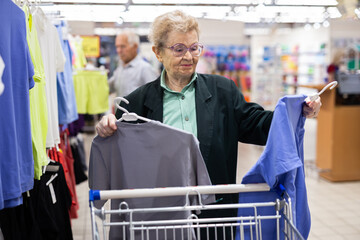 older woman with glasses chooses blouse in clothing department of supermarket