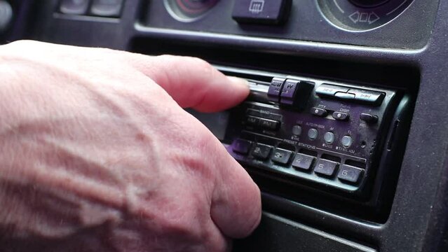 The driver inserts a cassette into a cassette recorder in an old car.	