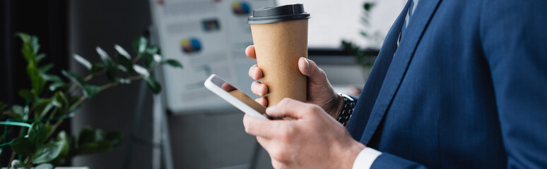 cropped view of economist with coffee to go messaging on mobile phone in office, banner.
