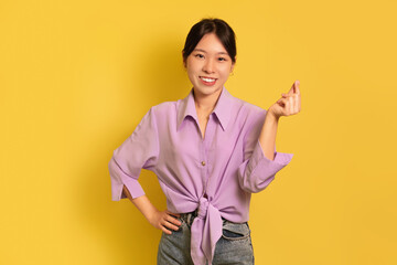 Happy young Asian lady holding invisible object in hand on yellow studio background, mockup