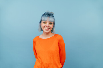 Smiling hipster girl with colored hair stands on a blue background with a happy face and looks at the camera.