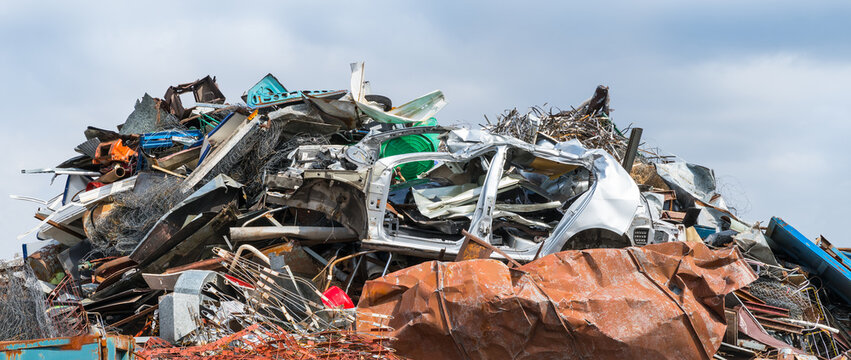 Close-up of mixed scrap metal pile in junkyard on panoramic blue sky background. Colored jumble of iron waste as old car body, wire mesh or rusty sheet and various leftover recyclable materials. Dump.
