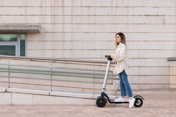 Side view of young woman riding a sustainable electric scooter in the city in front of a white building with copy space