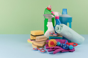 Different cleaning products against green and blue wall background with copy space. Cleaning service concept. Spray bottles with detergents and household chemicals. Mockup image