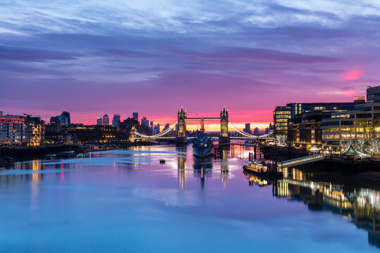 Tower Bridge and HMS Belfast reflecting in a still River Thames at sunset, London