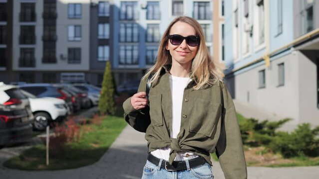 Beautiful blonde woman walking in the city. Fun happy young girl in sunglasses shake her head to make hair flying. Attractive young female lady turns around and looks into the camera outdoors.