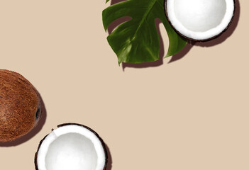 Summer fruit concept. Top view photo. Fresh and halved coconuts with monstera leaf on beige backdrop