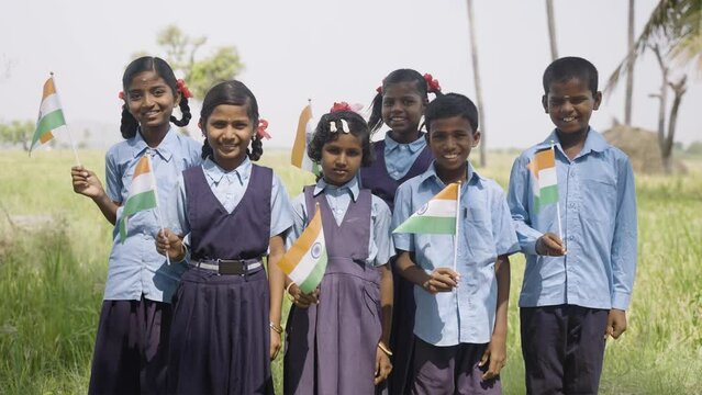 group of happy smiling viallge school kids in unifrom holding Infian flag by looking at camera during independence day celebrations - conept of patriotismsm, diversity and real people.