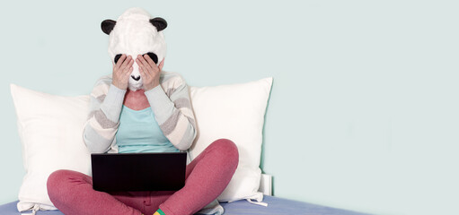 woman working in panda mask sitting in front of the laptop on bed. hands covering her face....