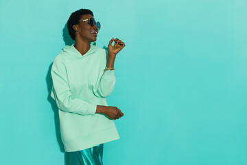 Young black woman in pastel mint sweatshirt and sunglasses is looking to the side and laughing.