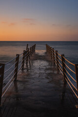 Obraz premium Jetty at pebbles beach near Canico at Portugese Madeira Island at sunrise time. October 2021. Long exposure picture