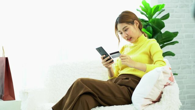 Asian women hold credit cards using digital mobile devices and shop online, type bank card numbers on smartphones, and transact using mobile banking applications. online shopping concept