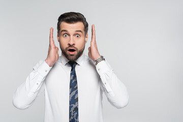 shocked businessman holding hands near face and looking at camera isolated on grey.