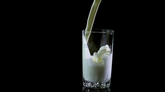 Pouring milk into a glass on balck background. Slow motion