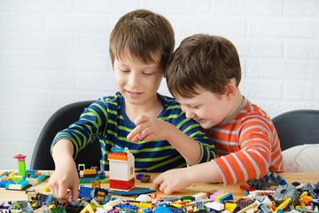 Two boys are assembling a constructor together, building something. There are many details on the table. Children enjoy doing interesting things.