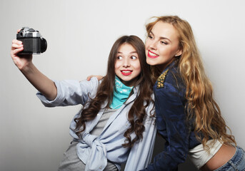 Happy young female friends taking some pictures, with camera, over grey background