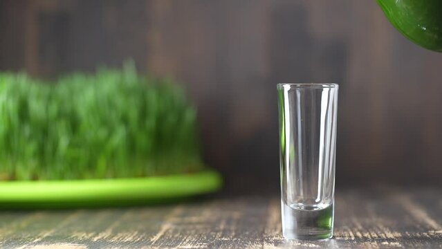 Healthy organic green detox juice from grass of green germinated wheat grains, close up, slow motion.  Green leaves of young wheat and wheatgrass juice pouring into a glass
