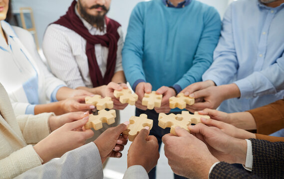 Diverse team of business people joining pieces of wooden jigsaw puzzle. Group of men and women putting jigsaw parts together as metaphor for teamwork, synergy and problem solving
