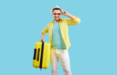 Joyfully excited young male traveler with suitcase isolated on vivid light blue background....