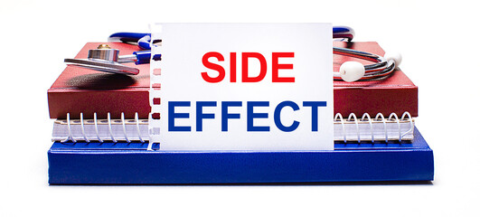 On a light background notepad, a stethoscope and a white card with the text SIDE EFFECT. Medical...