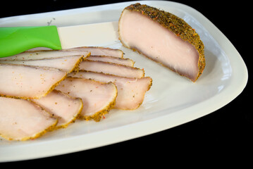 Sliced pieces of dried meat with spices on a white plate on a black background